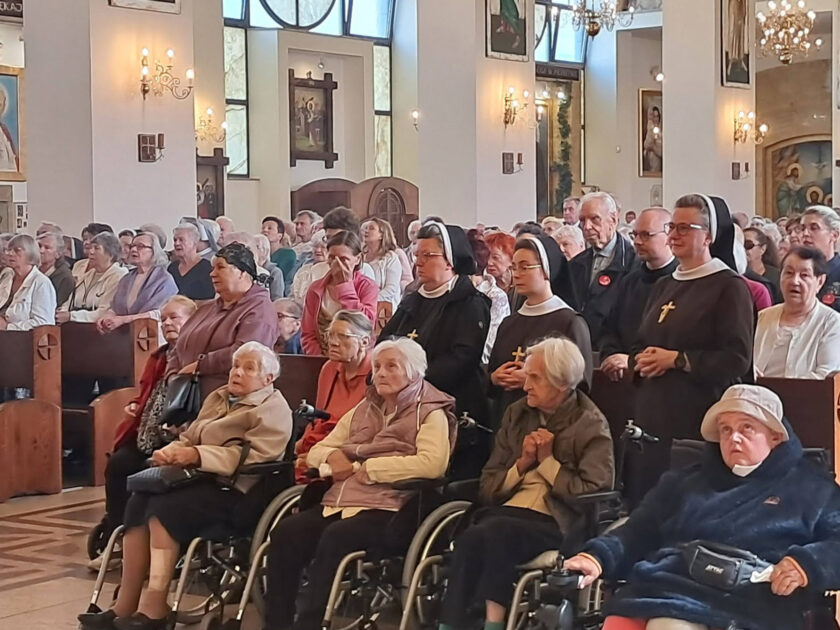 Licznie zgromadzeni wierni podczas nabożeństwa w kościele. W pierwszych rzędach znajdują się seniorzy, w tym osoby poruszające się na wózkach.