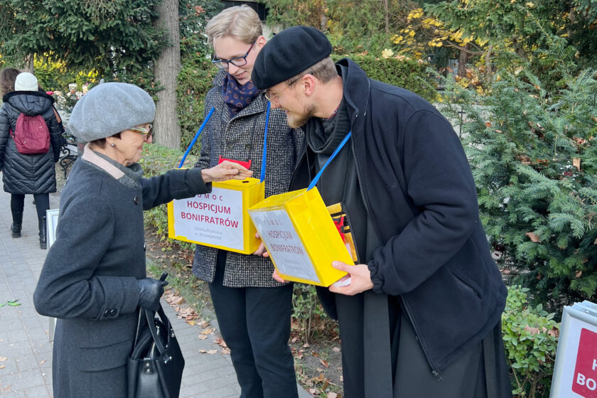 Starsza kobieta przekazuje datek do puszki kwestarskiej trzymanej przez wolontariusza. Obok stoi drugi wolontariusz uczestniczący w zbiórce na rzecz Hospicjum Bonifratrów.